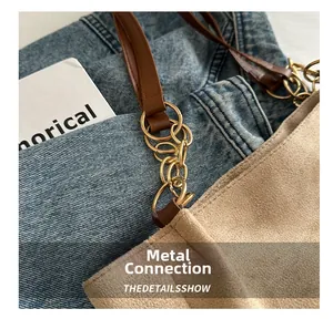 Detail of camel suede tote bag with golden metal chain links and brown leather handles