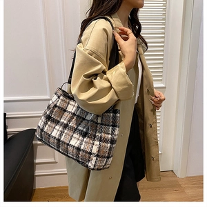 Fashionable large tweed tote bag with black leather straps worn by model in a chic room