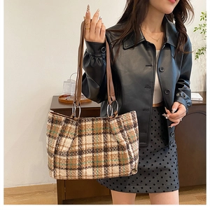Close-up of a large plaid tote bag with brown straps and silver ring hardware details