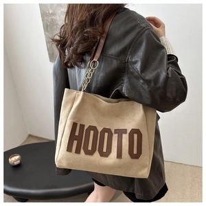 Dettaglio della borsa tote beige con lettere HOOTO marroni e tracolla a catena dorata