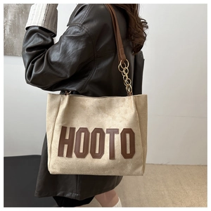 Detail of beige tote bag with brown HOOTO lettering and gold chain strap detail