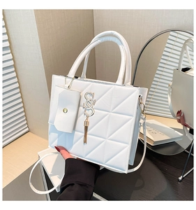 Close-up of white quilted handbag with triangle stitching and golden logo charm