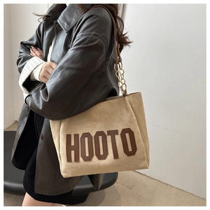 Detail of light khaki tote bag featuring dark HOOTO lettering and metal chain strap