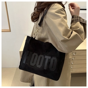 Detail of black tote bag with HOOTO letter patch and gold metal chain strap on model