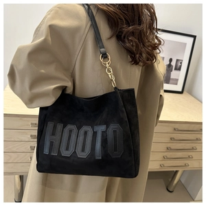 Detail of black suede tote bag featuring metallic chain strap and HOOTO logo