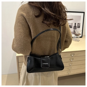 Glossy black crescent shoulder bag with magnetic flap closure shown in a lifestyle setting