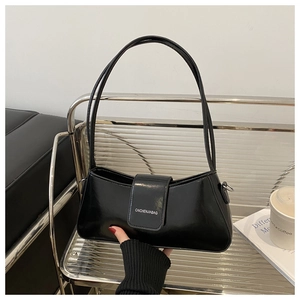 Detail of minimalist black patent leather crescent bag on a glass shelf with accessories