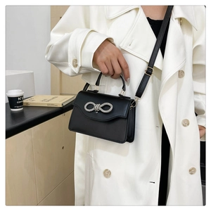 Detail of a black mini crossbody bag with a sparkling rhinestone bow on a white coat