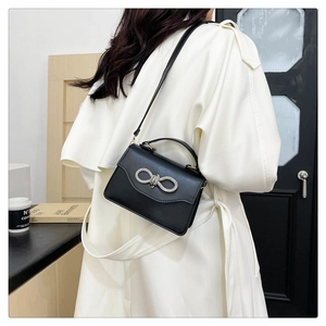 Detail of elegant black leather crossbody bag with rhinestone bow on white trench coat