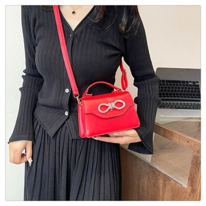 Detail of red leather crossbody bag with silver rhinestone bow and adjustable strap