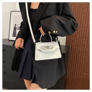 Close-up of white glossy crossbody bag featuring a sparkling rhinestone bow detail