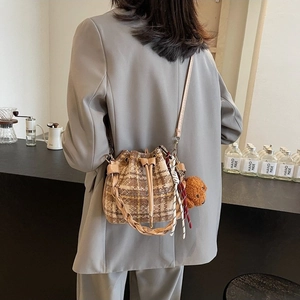 Brown plaid drawstring bucket bag with bear pendant shown on model in a cafe