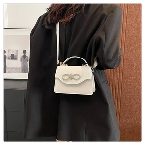 Detail showing the white crossbody bag with a sparkling rhinestone bow buckle and top handle