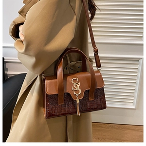 Detail of crocodile pattern leather handbag with gold tassel and SS logo on model