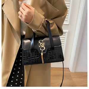 Detail of black crocodile texture handbag with gold tassel and metal logo hardware