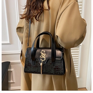 Detail view of black handbag with crocodile pattern and golden metal tassel logo