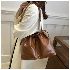 Brown soft leather bucket bag detail showing the elegant slouchy design and chic bow accent.