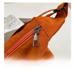 Detailed macro shot of the smooth nylon fabric and durable metal zipper on the orange bag