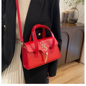 Detail of red croc-embossed leather handbag with gold S-buckle and elegant tassel