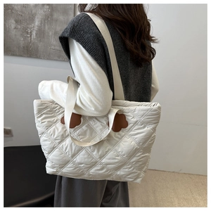 Quilted white tote bag with floral accents shown on shoulder in minimalist studio