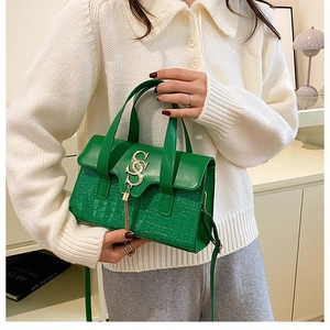 Close-up of green crocodile texture handbag with gold tassel and metal buckle detail