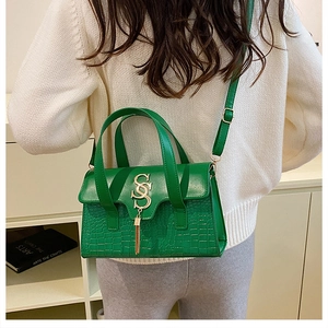 Close-up of green crocodile texture bag with gold SS logo and tassel worn by model
