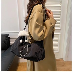 Detail of black pleated nylon shoulder bag with white cloud charm on khaki coat