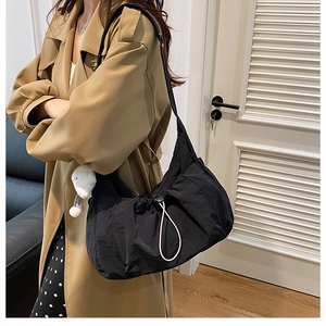 Close-up of black nylon crescent shoulder bag with drawstring detail and plush charm