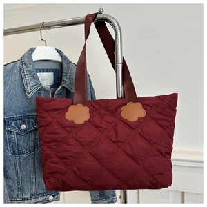 Detail of burgundy quilted tote bag featuring diamond pattern and floral strap accent