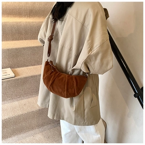 Détail du sac croissant en daim marron foncé avec plis verticaux et nœud sur la bandoulière