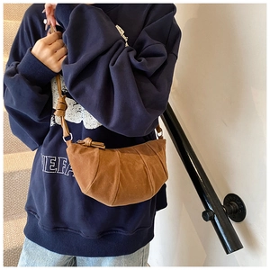 Détail du sac croissant en daim caramel montrant les plis et la sangle nouée à la main