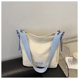 Détail du sac fourre-tout en toile avec lanières en cuir bleu clair sur un coussin noir
