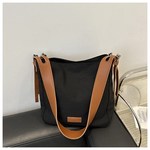 Détail du sac fourre-tout en toile noire avec bandoulière en cuir marron et étiquette