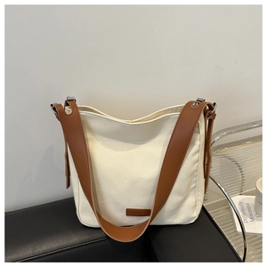 Détail du cabas en toile crème avec bandoulière en cuir marron sur un banc en cuir noir