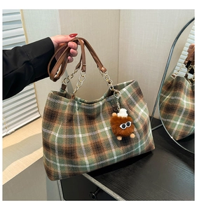 Detail of vintage plaid tote bag with brown leather handle and cute monster charm accessory