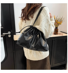 Close-up of black pleated bucket bag featuring a metallic bow and drawstring closure