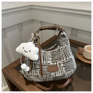 Detail of plaid woven shoulder bag featuring faux leather straps and a plush cloud charm