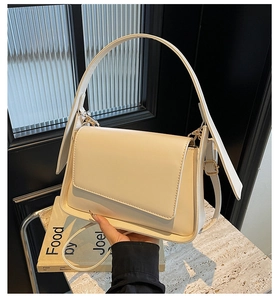 Detail van een beige lederen schoudertas met een gouden gesp en elegant handvat