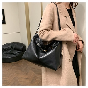 Close-up of a large black leather hobo bag side buckle on a model in a beige coat