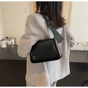 Minimalistische zwarte leren onderarmtas gedragen door een model in grijze blazer
