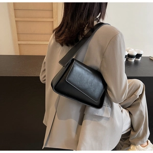 Minimalistische zwarte matlederen crossbodytas met brede schouderriem gedragen door model