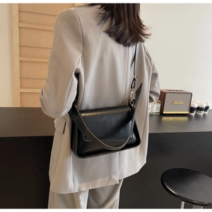 Rear view of model wearing minimalist black faux leather flap bag in a cafe setting
