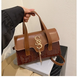 Detail of a brown leather handbag with croc-embossed texture and golden logo hardware