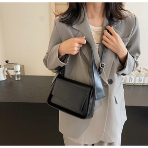 Minimalist black leather shoulder bag with flap closure worn by a model in a modern setting
