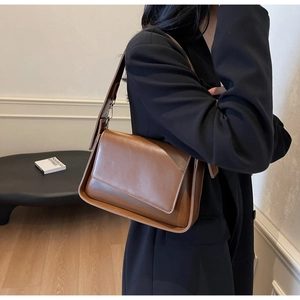 Detail view of brown matte leather shoulder bag with asymmetrical flap and wide strap