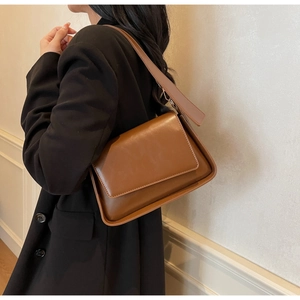 Detail view of a dark brown glossy leather crossbody bag worn over a black blazer