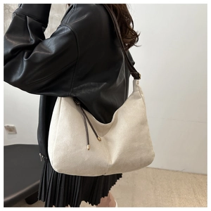Detail view of cream suede hobo bag with contrast straps and metal accents on model