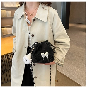 Detail view of a black bucket bag with a metal butterfly logo and plush charm