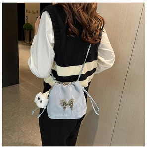 Detail of light blue bucket bag with silver butterfly knot and white plush ball charm