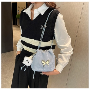 Detail of light blue bucket bag with butterfly gold buckle and plush charm on chain strap
